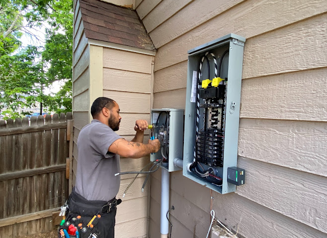 An electrician terminating conductors inside an open 200-amp panel.